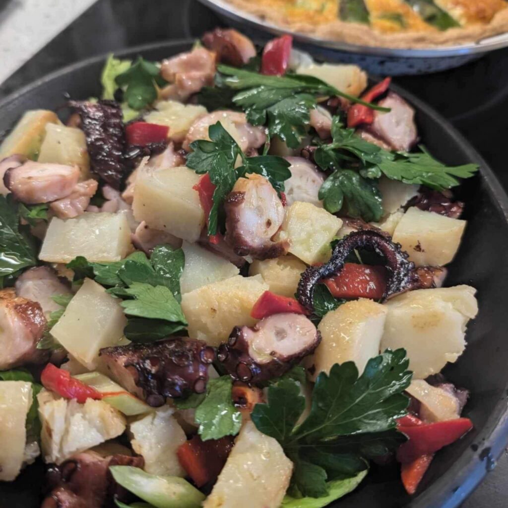 black plate with a colourful salad with potato and octopus