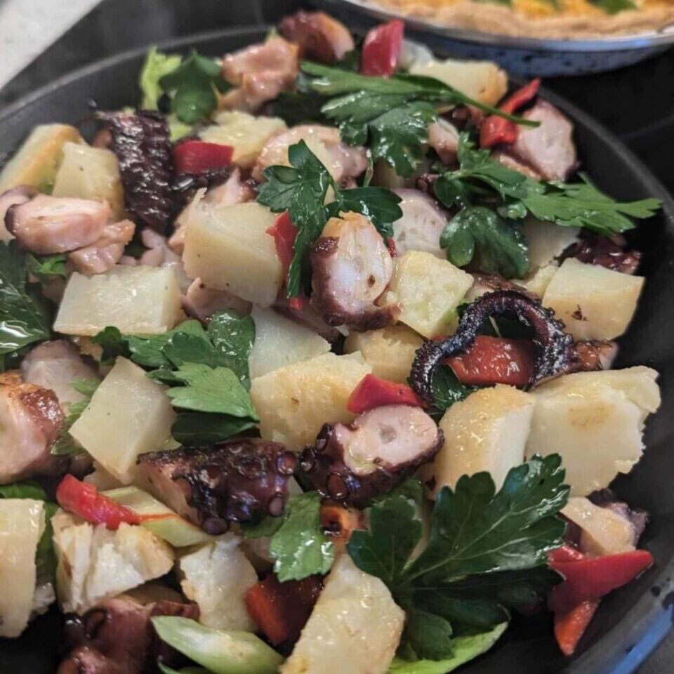 black plate with a colourful salad with potato and octopus