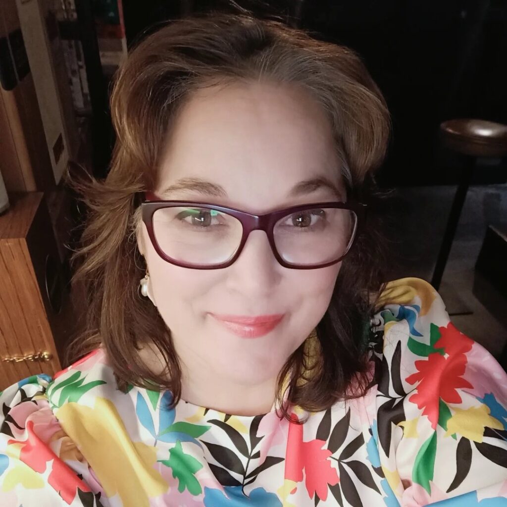 photo of a woman with dark hair wearing a coloufrul top and glasses