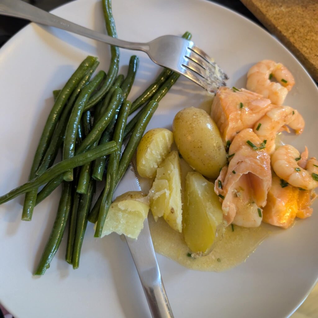 photo of a white plate with salmon, potatoes, and green beans, knife and fork