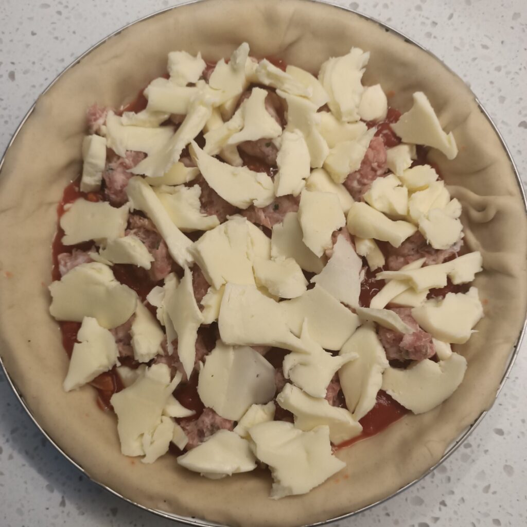 photo of an uncooked pie topped with cheese