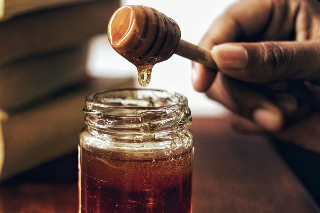 photo of a close up of a honey jar with a man's hand holding a honey stirrer