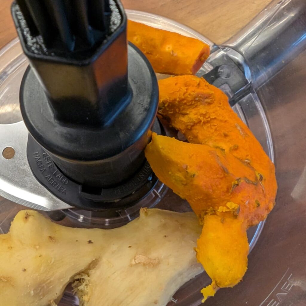 photo of a close up of a food processor with turmeric and ginger root