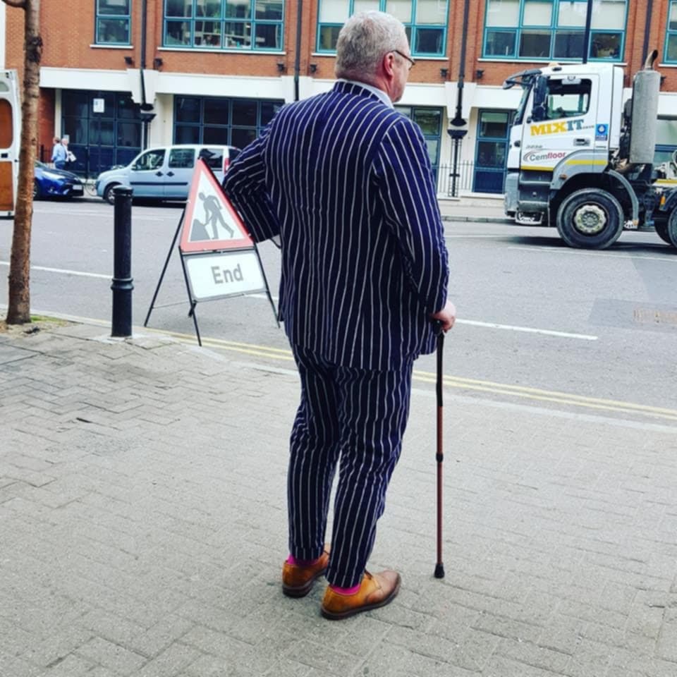 a photo of a man in a navy blue pinstripe suit with a walking stick in one hand standing on the street