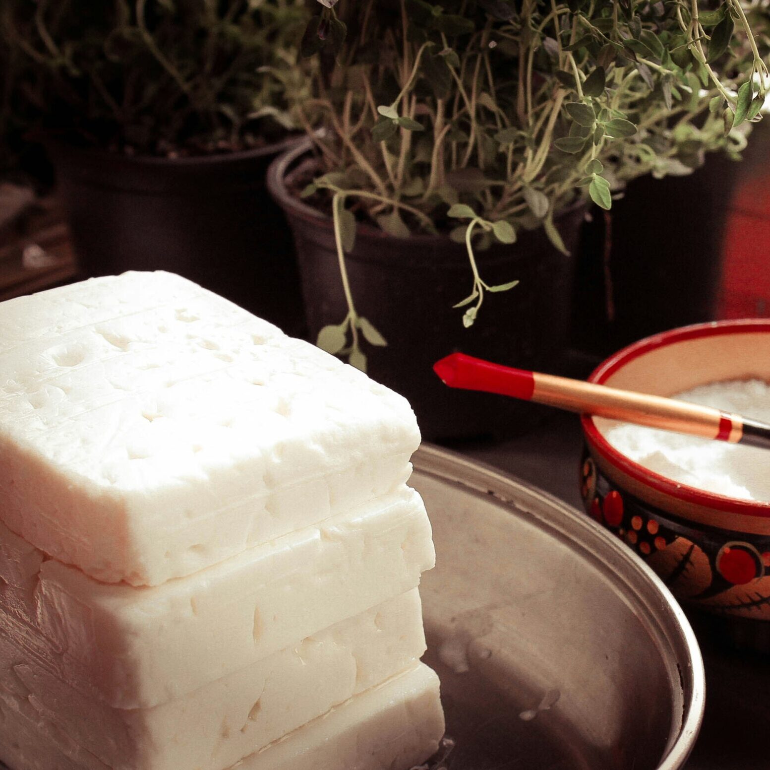 photo of a kitchen bench with blocks of feta cheese and bowl of salt and herbs in background