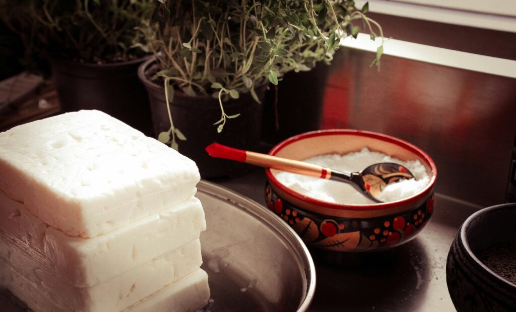 photo of a kitchen bench with blocks of feta cheese and bowl of salt and herbs in background