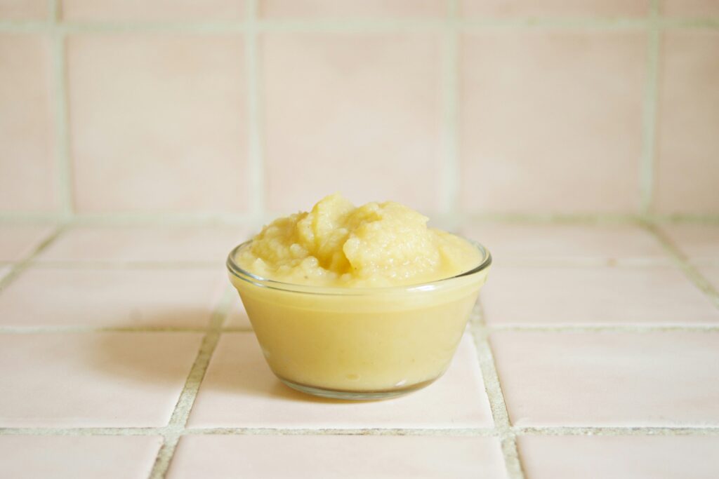 photo of apple sauce in a glass bowl against a white tiled background