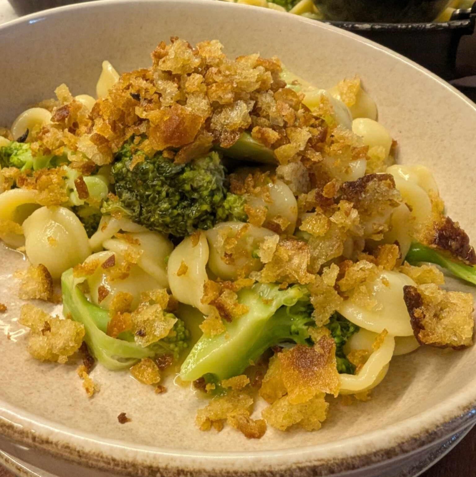 a photo of a bowl of pasta with broccoli and small round pasta topped with golden breadcrumbs