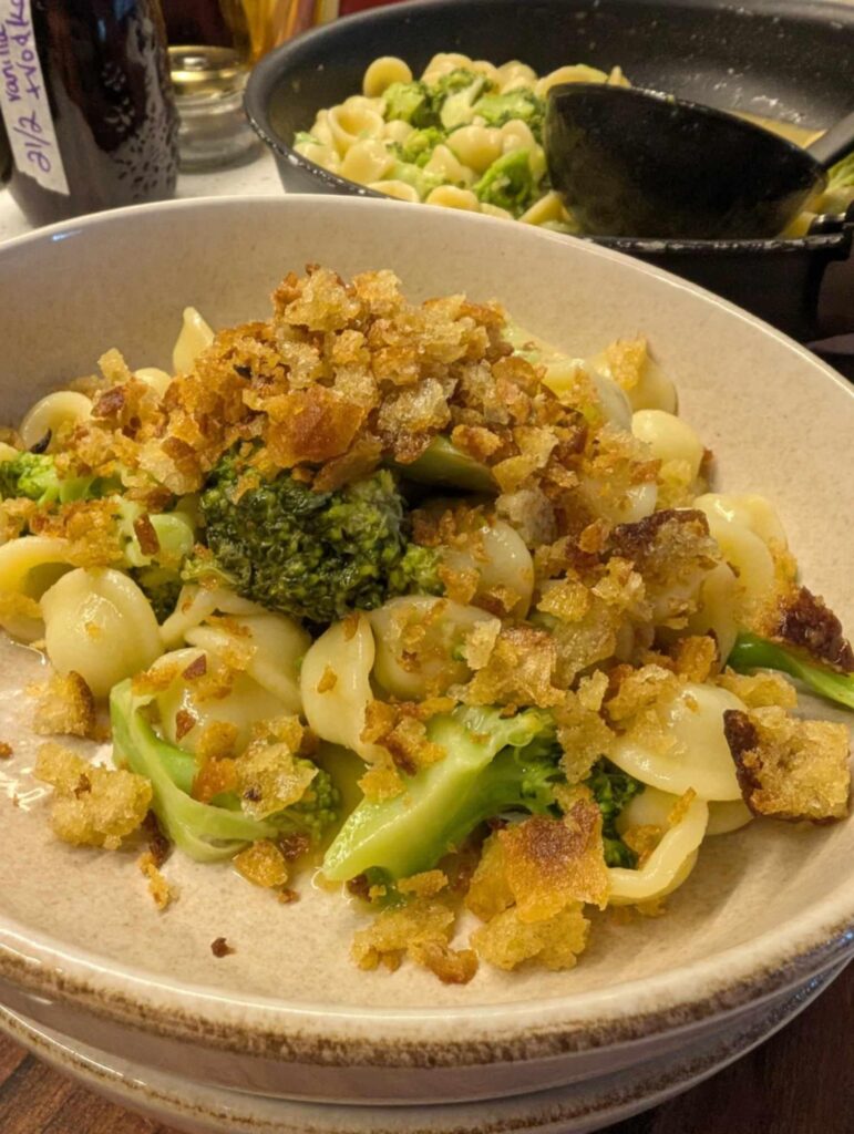 a photo of a bowl of pasta with broccoli and small round pasta topped with golden breadcrumbs