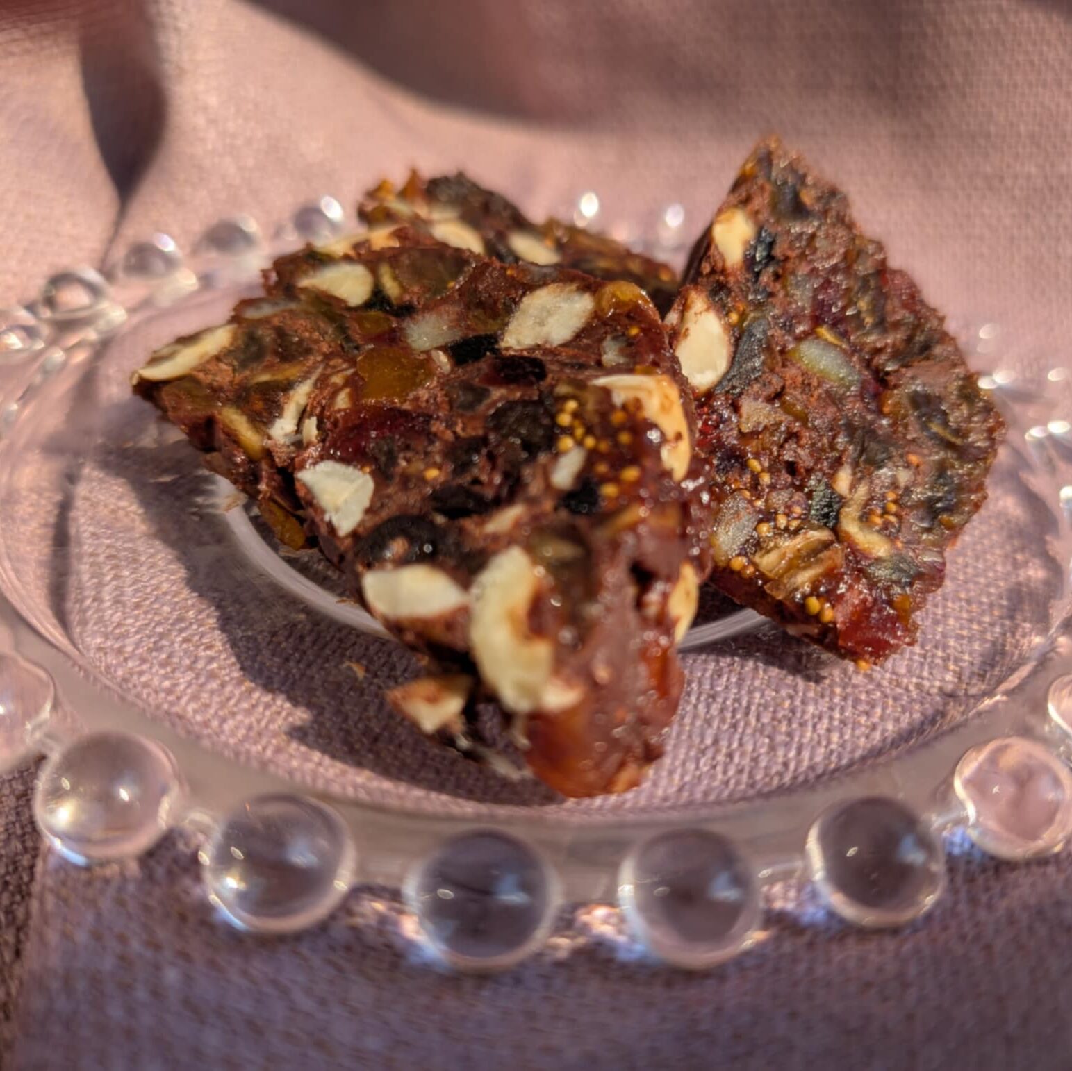 photo of chocolate slice with nuts and dried fruit on a glass plate with a mauve background