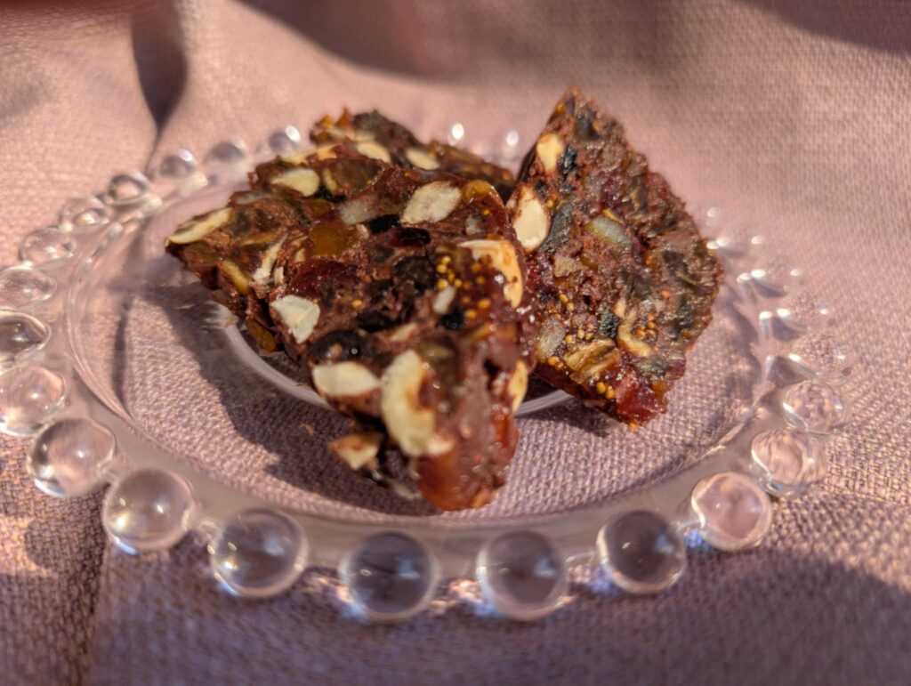 photo of chocolate slice with nuts and dried fruit on a glass plate with a mauve background