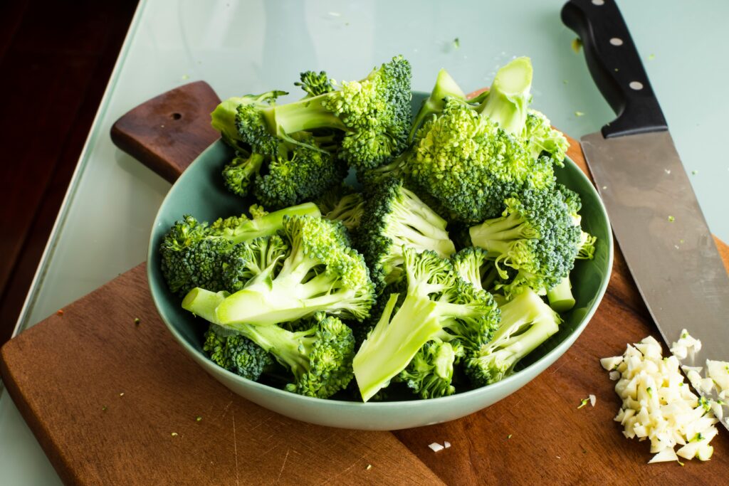 a bowl of broccoli florets resting on a dark brwon wooden board and a knife on the right