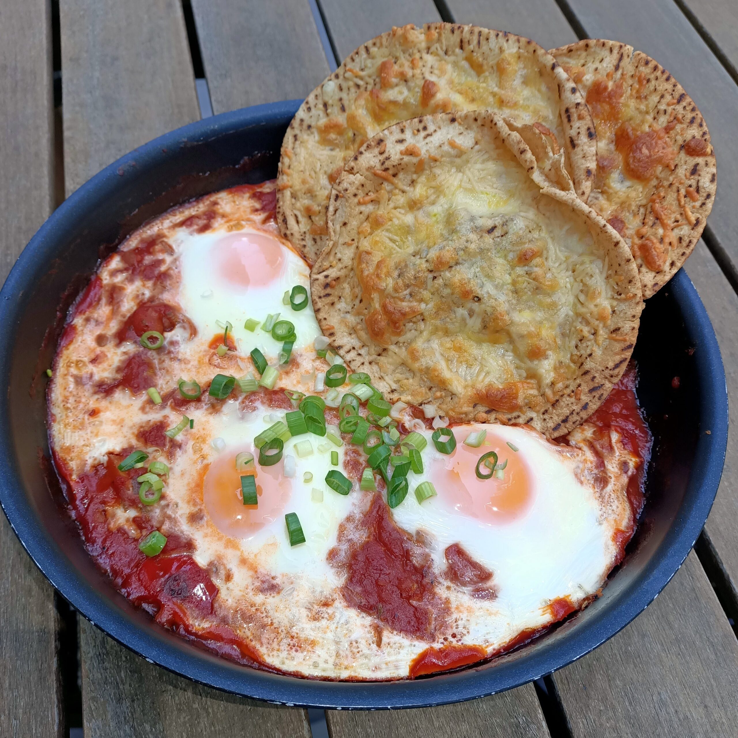 photo of cooked eggs in tomato in a fry pan with crispy bread on side